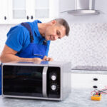 Side View Of Mature Man Repairing Microwave Oven In Kitchen